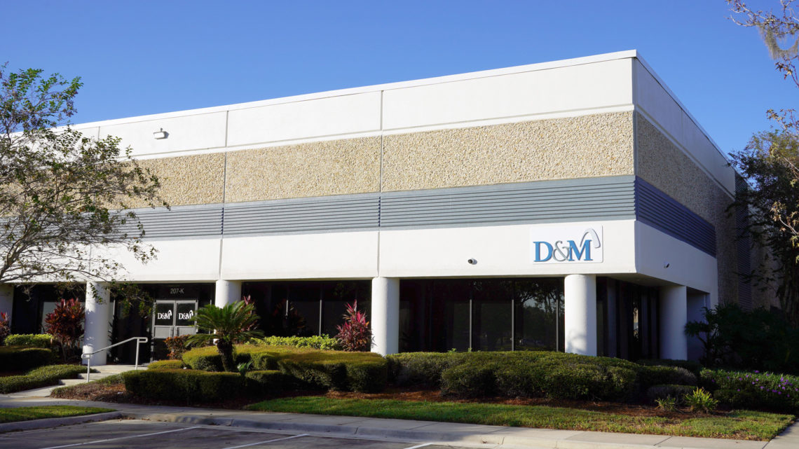 An image of the front of D&M Manufacturing building with bushes and trees.